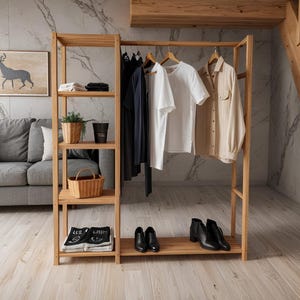 Op de afbeelding: Een houten kledingrek met planken, met opgevouwen kleding, een rieten mand en potplanten. Witte en beige shirts en een marineblauw kledingstuk hangen eraan. Zwarte enkellaarsjes en nette schoenen staan op de onderste plank.