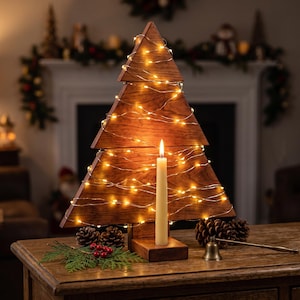 Op de afbeelding: Een driehoekige houten kerstboomdecoratie met een donkerbruine afwerking, omwikkeld met dunne gouden kerstverlichting. Een crèmekleurige dinerkaars staat in een houten voet aan de voorzijde, vergezeld door dennenappels en groene takjes.
