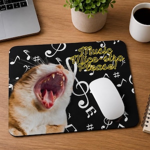 Op de afbeelding: Een rechthoekige muismat met een zwarte achtergrond voorzien van witte muzieknoten en symbolen. Een rood-witte kat is afgebeeld met de bek wijd open. De tekst "Music Mice-stro Please!" staat in het geel aan de rechterkant gedrukt.