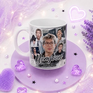 Könnte beinhalten: Ein weißer Keramikbecher mit einer Fotocollage des Musikers Namjoon. Das Design enthält den Namen Namjoon in Schreibschrift, koreanischen Text und verschiedene Bilder des Künstlers. Der Becher hat einen Henkel auf der linken Seite.
