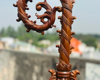 May include: A detailed, hand-carved wooden staff with a spiral top and ornate floral and scrollwork designs. The staff is a rich brown color and features intricate carvings along its length and at the base.