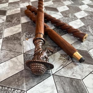 May include: Several wooden walking canes with a spiral design. One cane has a detailed bronze-colored handle with a basket-like design and a figure on top. The canes are brown and have a brass-colored tip.