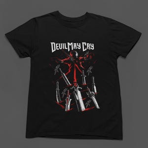 May include: A black short-sleeved t-shirt featuring a graphic print with the text Devil May Cry at the top. The design displays a central figure in red and white, surrounded by multiple sword illustrations and red slash marks on a black background.