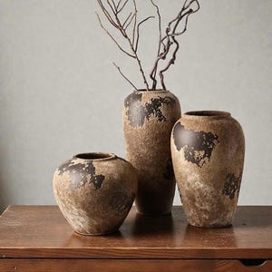 Puede incluir: Tres jarrones decorativos con un acabado envejecido y texturizado en tonos marrón y marrón oscuro. Los jarrones varían en tamaño y forma, con un jarrón alto que contiene ramas secas. Decoración del hogar.