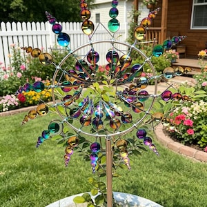 Könnte beinhalten: Ein farbenfroher, schillernder Metall-Gartenspinner mit Sonnenstrahlendesign. Der Spinner hat mehrere Reihen schillernder Glaskugeln und Tropfenformen, die auf einer Metallstange montiert sind. Die Gartenkunst steht in einem weißen Betonpflanzgefäß.