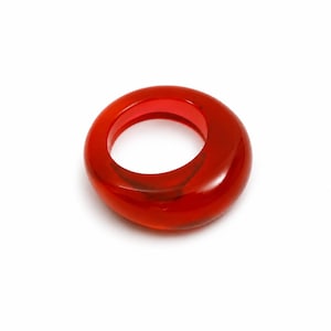 May include: A translucent, vibrant red ring with a smooth, rounded, and asymmetrical organic shape. The band features a polished finish that catches the light, creating depth and clarity within the solid, glossy red material of the ring.