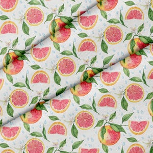 Könnte beinhalten: Ein weißer Stoff mit einem sich wiederholenden Aquarellmuster aus rosa Grapefruitscheiben, ganzen Grapefruits, grünen Blättern, kleinen weißen Blüten und verstreuten blauen Wassertropfen auf der gesamten Oberfläche des Textilmaterials.