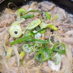 Peut inclure: Un bol noir contenant du bulgogi, un plat coréen composé de fines tranches de bœuf mariné, de nouilles de verre translucides et de lamelles d'oignon dans un bouillon savoureux, garni de rondelles d'oignons verts frais et de graines de sésame.