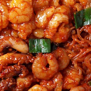 Könnte beinhalten: Ein scharfes koreanisches Pfannengericht mit Oktopus, Garnelen und durchscheinenden Glasnudeln in einer leuchtend roten Chilisauce, garniert mit gehackten Frühlingszwiebeln. Die Zutaten sind in einer reichhaltigen, glänzenden und strukturierten Sauce vermengt.