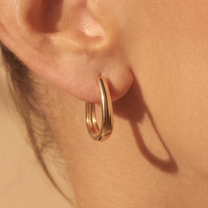 Könnte beinhalten: Ein kleiner, polierter Gold-Creolen-Ohrring mit einer glatten, abgerundeten Oberfläche. Der Ohrring hat ein durchgehendes, kreisförmiges Design, das sicher im Ohrläppchen sitzt und das Licht mit einem warmen, metallischen Glanz reflektiert.