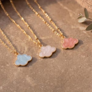 Puede incluir: Tres collares dorados, cada uno con un pequeño colgante en forma de nube. Los colgantes están rellenos de esmalte en azul claro, rosa pálido y un rosa más oscuro. Cada collar tiene una delicada cadena dorada de eslabones simples.