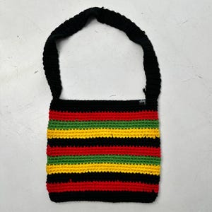 May include: A handmade crochet shoulder bag with a black strap and body. The bag features horizontal stripes in red, yellow, green, and black. The bag is made of a soft, textured yarn.