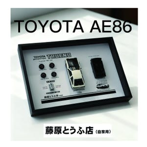 Op de afbeelding: Een ingelijste display met een wit en zwart Toyota AE86 modelauto, wielen en motoronderdelen. De tekst "TOYOTA AE86" staat bovenaan. De display bevat de tekst "TOYOTA TRUENO" en "AE86".