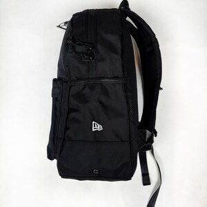 Puede incluir: Una mochila negra con exterior de tela texturizada, un bolsillo lateral y un logotipo de New Era blanco bordado en el lateral inferior. La bolsa incluye tiradores de cremallera negros, un panel trasero de malla acolchado y correas ajustables.