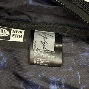 Puede incluir: Un bolso de tela negra con un estampado floral azul, que incluye una etiqueta de la marca New Era y una etiqueta de cuidado con instrucciones como no usar lej&iacute;a, no secar en secadora, no planchar y no lavar en seco.