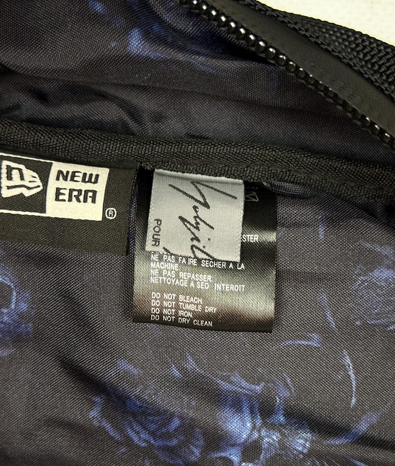 Puede incluir: Un bolso de tela negra con un estampado floral azul, que incluye una etiqueta de la marca New Era y una etiqueta de cuidado con instrucciones como no usar lej&iacute;a, no secar en secadora, no planchar y no lavar en seco.