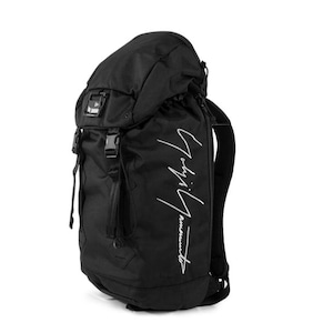 May include: Black backpack with a top flap, buckles, and a drawstring closure. The bag features a white script logo on the side. The backpack has adjustable shoulder straps and a padded back panel.