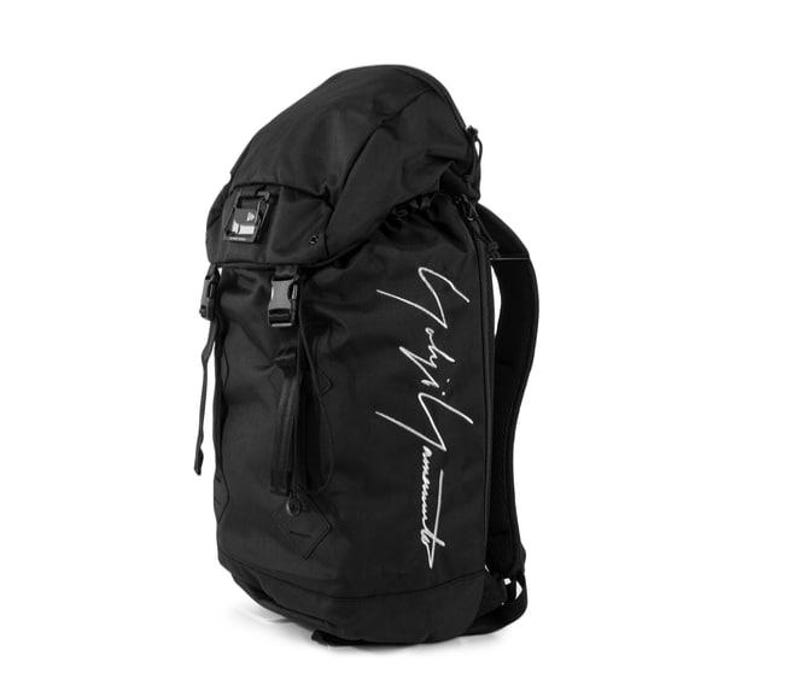 May include: Black backpack with a top flap, buckles, and a drawstring closure. The bag features a white script logo on the side. The backpack has adjustable shoulder straps and a padded back panel.