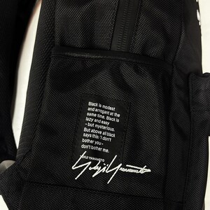 Puede incluir: Una mochila negra que presenta un parche de tela rectangular con texto blanco que dice: Black is modest and arrogant at the same time. Black is lazy and easy - but mysterious. But above all black says this: I don't bother you-don't bother me.