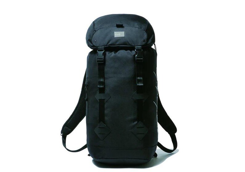 May include: A black backpack with a rounded top and adjustable straps. The backpack has multiple buckles and a small patch on the top. The shoulder straps are padded and curved. The bag is made of a durable material.