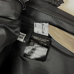 Peut inclure: L'int&eacute;rieur d'un sac en polyester noir avec une &eacute;tiquette de marque New Era et une &eacute;tiquette blanche portant le texte Comme des Gar&ccedil;ons. Une &eacute;tiquette d'entretien noire indique Fabriqu&eacute; au Vietnam, 100% Polyester et Ne pas blanchir.