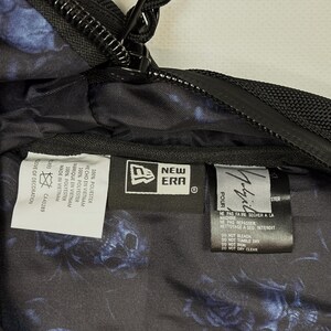 Puede incluir: El interior de una bolsa negra con un patr&oacute;n floral azul y varias etiquetas de tela. Las etiquetas muestran el logotipo de New Era, la marca Yohji Yamamoto e instrucciones de cuidado en ingl&eacute;s, franc&eacute;s y espa&ntilde;ol, incluyendo 100% poli&eacute;ster.