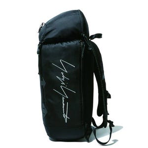 May include: Black backpack with a curved top and a zippered main compartment. The bag features a white script logo on the front and adjustable shoulder straps. The backpack is made of a durable material and is suitable for carrying various items.