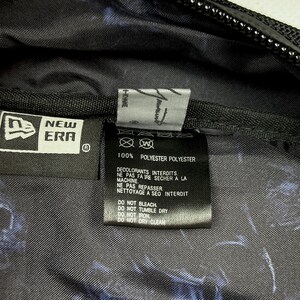 Puede incluir: El interior de una bolsa de poli&eacute;ster negra con una etiqueta de la marca New Era y una etiqueta de cuidado con instrucciones en franc&eacute;s e ingl&eacute;s. La tela tiene un patr&oacute;n abstracto en azul oscuro y negro. La etiqueta indica 100% poli&eacute;ster.