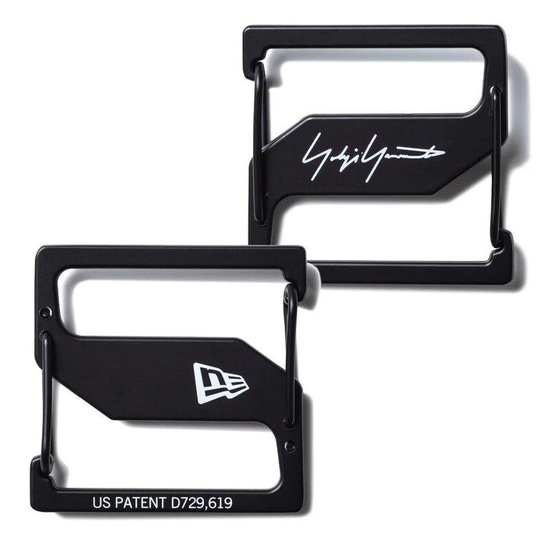 May include: Two black metal wallets with a rectangular frame design. One wallet features the white signature "Yohji Yamamoto", and the other displays the white "New Era" logo. The bottom wallet has the text "US PATENT D729,619".