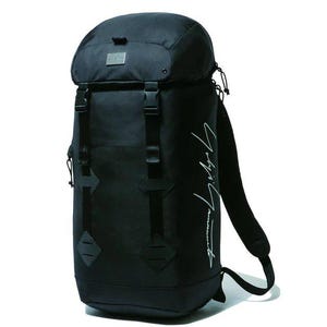 May include: Black backpack with a roll-top closure, adjustable straps, and multiple buckles. Features a small metal tag and white script on the side. The bag is designed for carrying items.