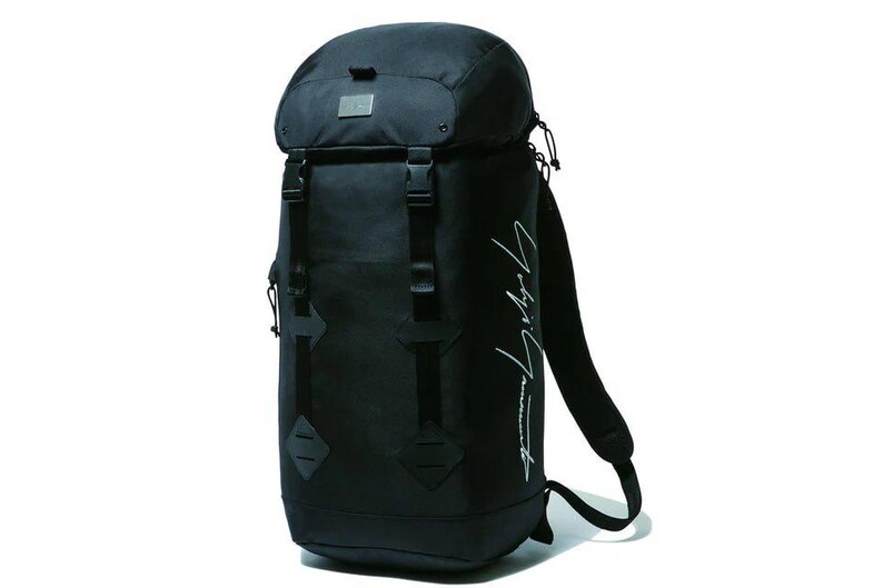 May include: Black backpack with a roll-top closure, adjustable straps, and multiple buckles. Features a small metal tag and white script on the side. The bag is designed for carrying items.