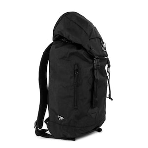 May include: Black backpack with a roll-top closure, side straps, and a front zippered pocket. The backpack has adjustable shoulder straps and a top handle. The New Era logo is visible on the lower front. The bag is made of a durable, textured material.