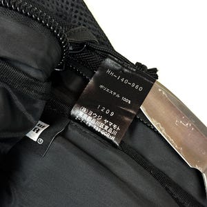 Peut inclure: Un sac en textile noir dot&eacute; d'une &eacute;tiquette d'entretien int&eacute;rieure bien visible avec le texte HH-140-960, 100% polyester, et des caract&egrave;res japonais incluant Yohji Yamamoto. Le sac pr&eacute;sente une section en maille noire, une fermeture &eacute;clair et une doublure en tissu noir lisse.