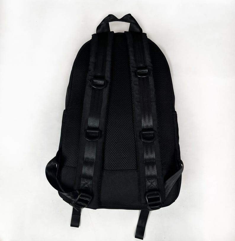 Puede incluir: Una mochila negra con panel trasero de malla acolchada, correas ajustables para los hombros con anillas en D integradas y un asa superior. El dise&ntilde;o incluye costuras reforzadas en las correas y un exterior de tela negra estructurada.