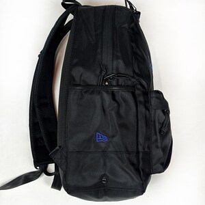 Peut inclure: Un sac &agrave; dos noir dot&eacute; d'un ext&eacute;rieur en tissu textur&eacute;, d'une poche lat&eacute;rale avec un petit logo brod&eacute; bleu et de bretelles rembourr&eacute;es r&eacute;glables. Le design comprend un compartiment avant zipp&eacute; et des tirettes de fermeture &eacute;clair noires.
