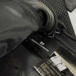 Peut inclure: L'int&eacute;rieur d'un sac noir avec une &eacute;tiquette d'entretien en tissu noir portant le texte blanc 100% POLYESTER, EXCLUSIVE OF DECORATION, DO NOT BLEACH, DO NOT TUMBLE DRY, DO NOT IRON, DO NOT DRY CLEAN. Une seconde &eacute;tiquette blanche est visible.