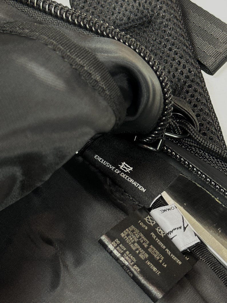 Peut inclure: L'int&eacute;rieur d'un sac noir avec une &eacute;tiquette d'entretien en tissu noir portant le texte blanc 100% POLYESTER, EXCLUSIVE OF DECORATION, DO NOT BLEACH, DO NOT TUMBLE DRY, DO NOT IRON, DO NOT DRY CLEAN. Une seconde &eacute;tiquette blanche est visible.
