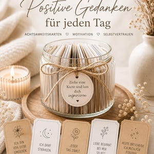 May include: A glass jar filled with cards, tied with twine and a round tag reading 'Ziehe eine Karte und lass dich inspirieren'. Five rectangular cards are displayed in front, each featuring a unique line drawing and German text, including 'Ich bin von Liebe umgeben', 'Ich darf strahlen', 'Jeder Tag zählt', 'Liebe beginnt bei mir selbst', and 'Heute entscheide ich mich für positive Gedanken'.