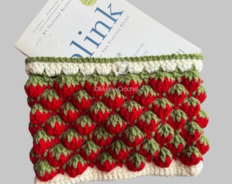 May include: A rectangular crochet pouch featuring a repeating strawberry pattern in red and green yarn. The pouch has a cream-coloured border at the top and bottom, a clear button closure, and contains a book titled Blink by Malcolm Gladwell.