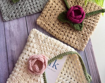 May include: Three square crochet envelopes in grey, tan, and cream, each featuring a green crocheted border and a three-dimensional crocheted flower in pink or dark magenta. The cream envelope is partially open, revealing a white card with text.