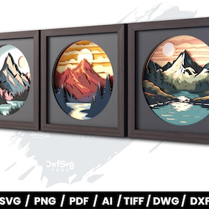 May include: Three framed wall art pieces featuring layered paper cut designs of mountain landscapes. Each piece has a circular mountain scene with a lake, trees, and a sun or moon. The frames are dark brown.