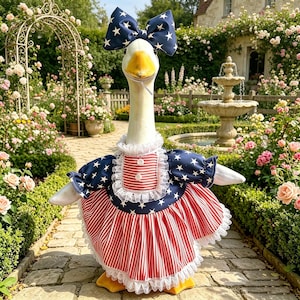 May include: A goose wearing a patriotic outfit with a large blue bow with white stars. The dress features red and white stripes and blue sleeves with white stars. The goose is standing in a garden with a fountain.