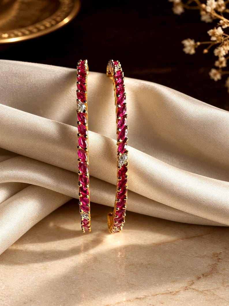 May include: Two gold bangles featuring a continuous row of marquise-cut vibrant pink stones. Each bangle is accented with small, clear, round-cut stones placed at intervals along the band, creating a repeating pattern of pink and clear gems.