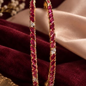 May include: Two gold bangles featuring a continuous row of marquise-cut vibrant pink stones interspersed with small, clear, round-cut white stones. The metal setting is polished gold, and the stones are arranged in a repeating pattern along the band.
