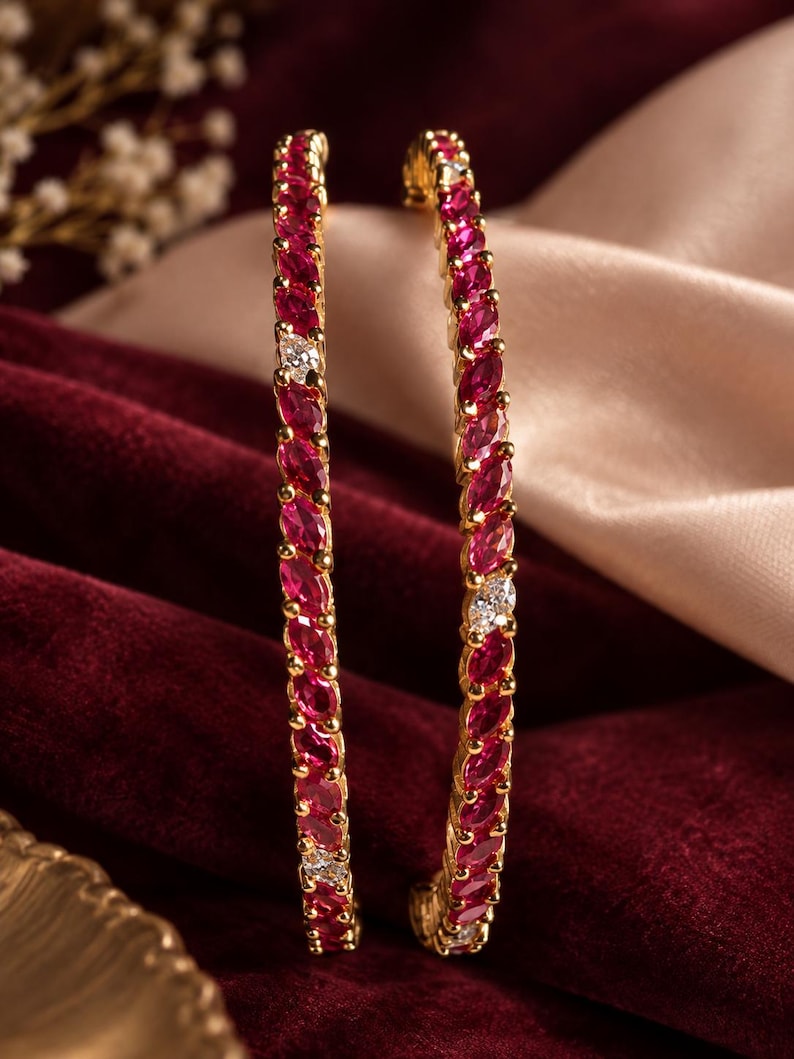May include: Two gold bangles featuring a continuous row of marquise-cut vibrant pink stones interspersed with small, clear, round-cut white stones. The metal setting is polished gold, and the stones are arranged in a repeating pattern along the band.