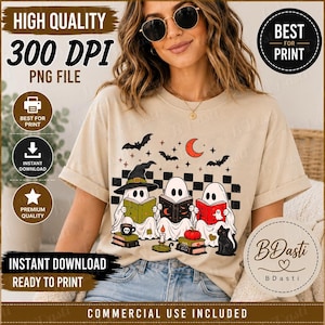 May include: A beige t-shirt featuring a graphic of three ghosts wearing hats and reading books, surrounded by bats, a crescent moon, stars, a pumpkin, a black cat, and a checkered pattern. The design includes text elements and various icons.