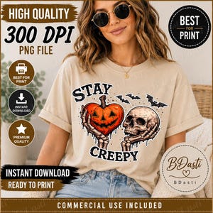May include: A beige t-shirt featuring a graphic print of two skeletal hands holding a heart-shaped orange jack-o'-lantern and a human skull. The text "STAY CREEPY" is printed in black above and below the graphic, accompanied by three small black bats.