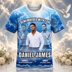 May include: A short-sleeve t-shirt featuring a blue sky and cloud background with a central photograph of a person in a white shirt. Text reads REMEMBERED WITH LOVE, DANIEL JAMES, SUNRISE 10 NOVEMBER, 1991, and SUNSET 21 APRIL, 2026.