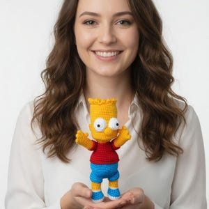 Peut inclure: Poupée Bart Simpson au crochet faite à la main, avec une peau jaune, un t-shirt rouge, un short bleu et des cheveux jaunes. La poupée a des yeux blancs et des bras tendus. Sur fond blanc.