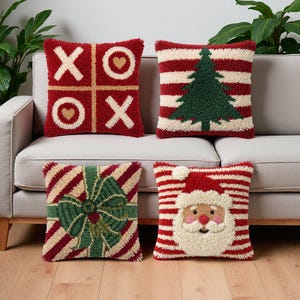 Könnte beinhalten: Vier quadratische Kissen mit strukturierter Punch-Needle-Stickerei. Eines zeigt ein rotes Gitter mit weißen X und goldenen Herzen. Ein weiteres hat rote und weiße Streifen mit einem grünen Tannenbaum. Eines zeigt eine grüne Schleife auf Streifen. Eines zeigt den Weihnachtsmann.